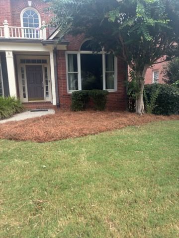 Brick house front entrance with white columns, arched window, and green lawn with mulched flower bed.
