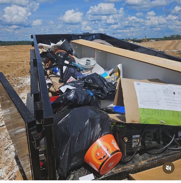 Trash piled in a dumpster on a construction site under a bright blue sky.