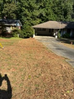 Suburban house with driveway and dry brown lawn beside trees