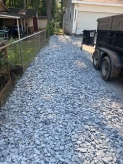 Gravel driveway beside a chain-link fence, with a trailer parked near a garage.