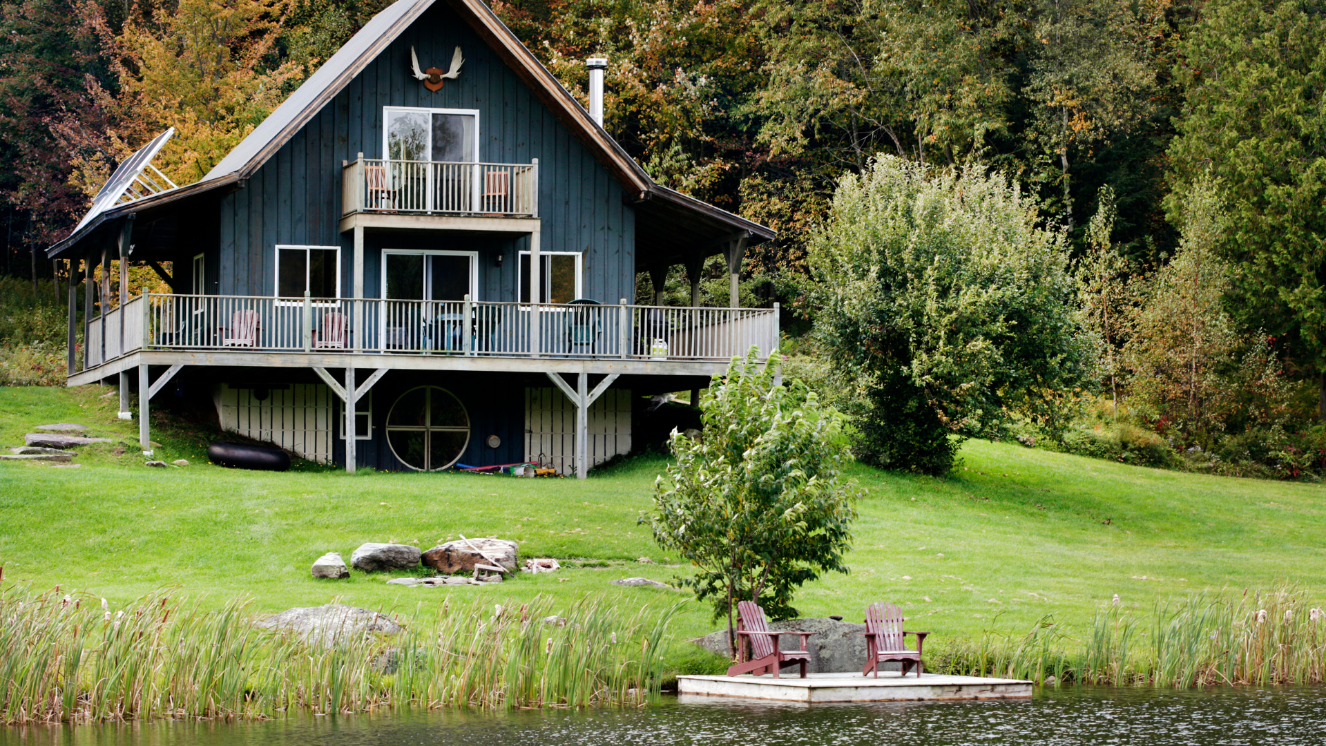 A large house is sitting on top of a lush green hill next to a lake.