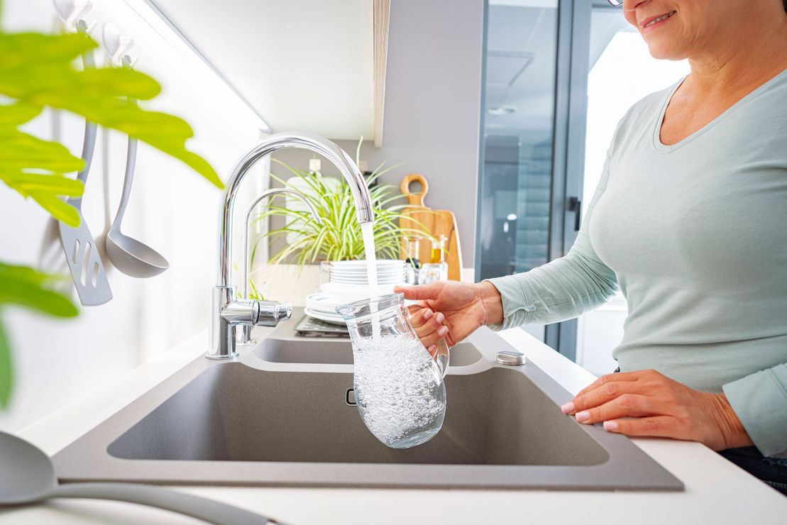 Una donna sta versando dell'acqua in un bicchiere nel lavandino della cucina.