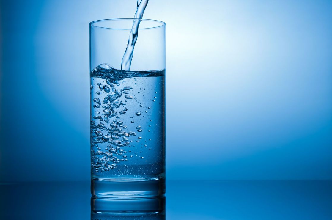 L'acqua viene versata in un bicchiere su uno sfondo blu.