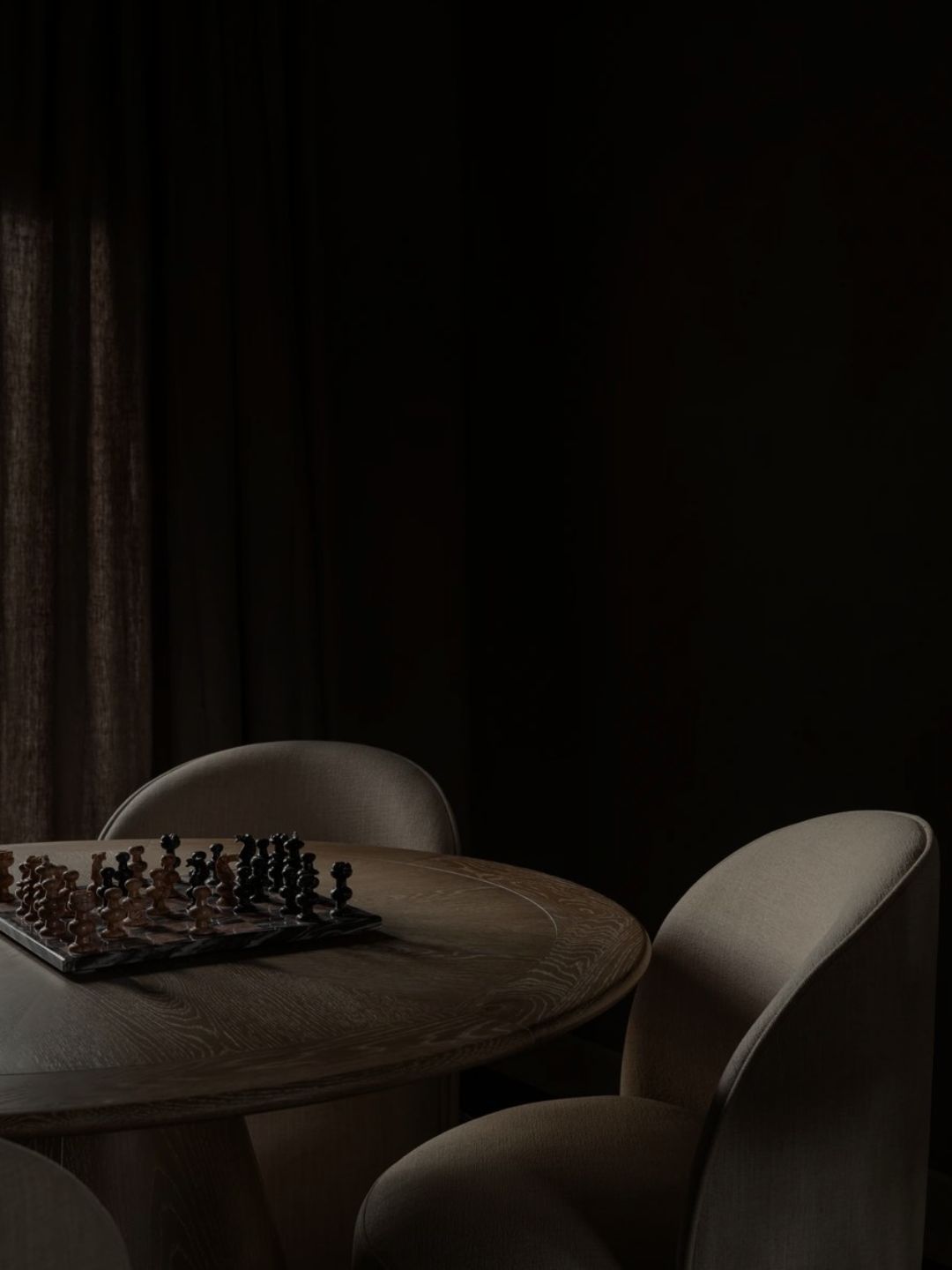 Een schaakbord op een ronde houten tafel naast een beige stoel in een schemerig verlichte kamer.