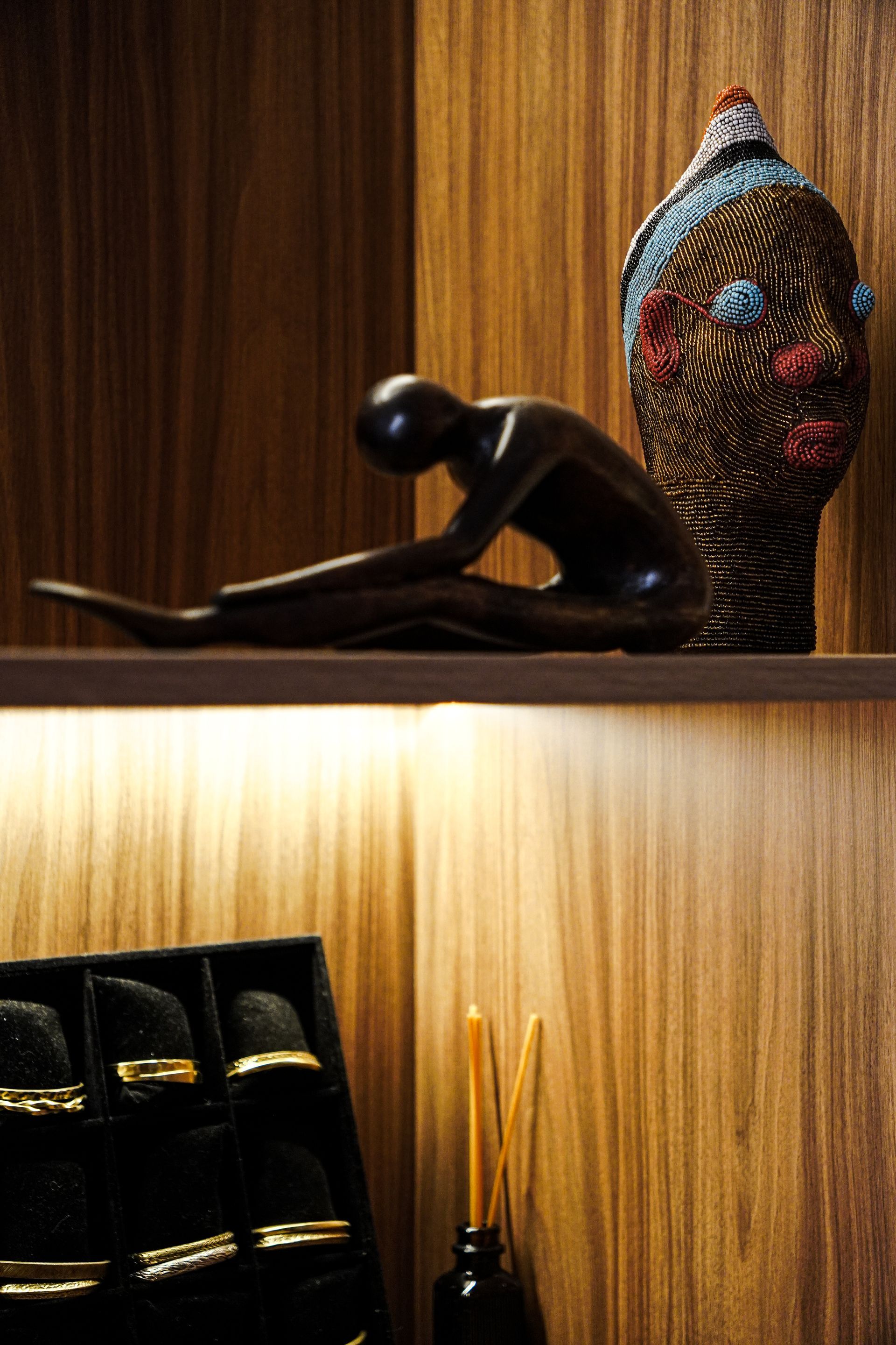 Decoratieve plank met een zwart beeldje, een geweven vaas, boeken en een kaars op een houten paneel.