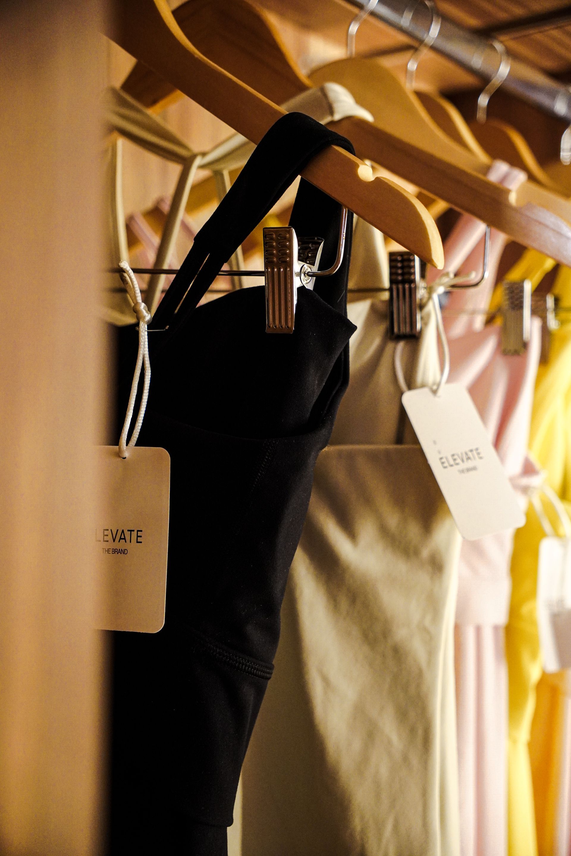 Kledingrek met zwarte, beige en gele kledingstukken aan houten hangers met prijskaartjes.