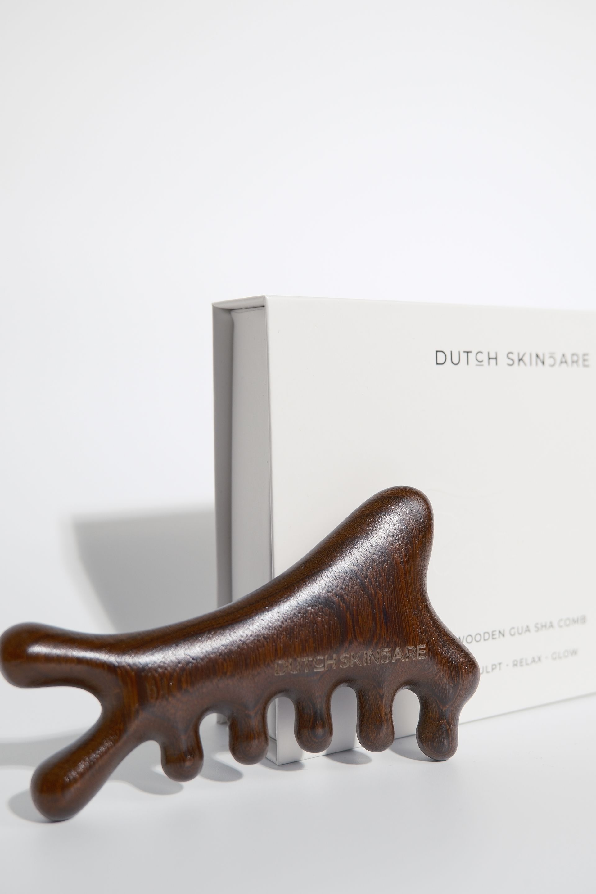 Bruine, hoofdvormige hoofdmassageapparaat voor een witte DUTCHSKINCARE-doos