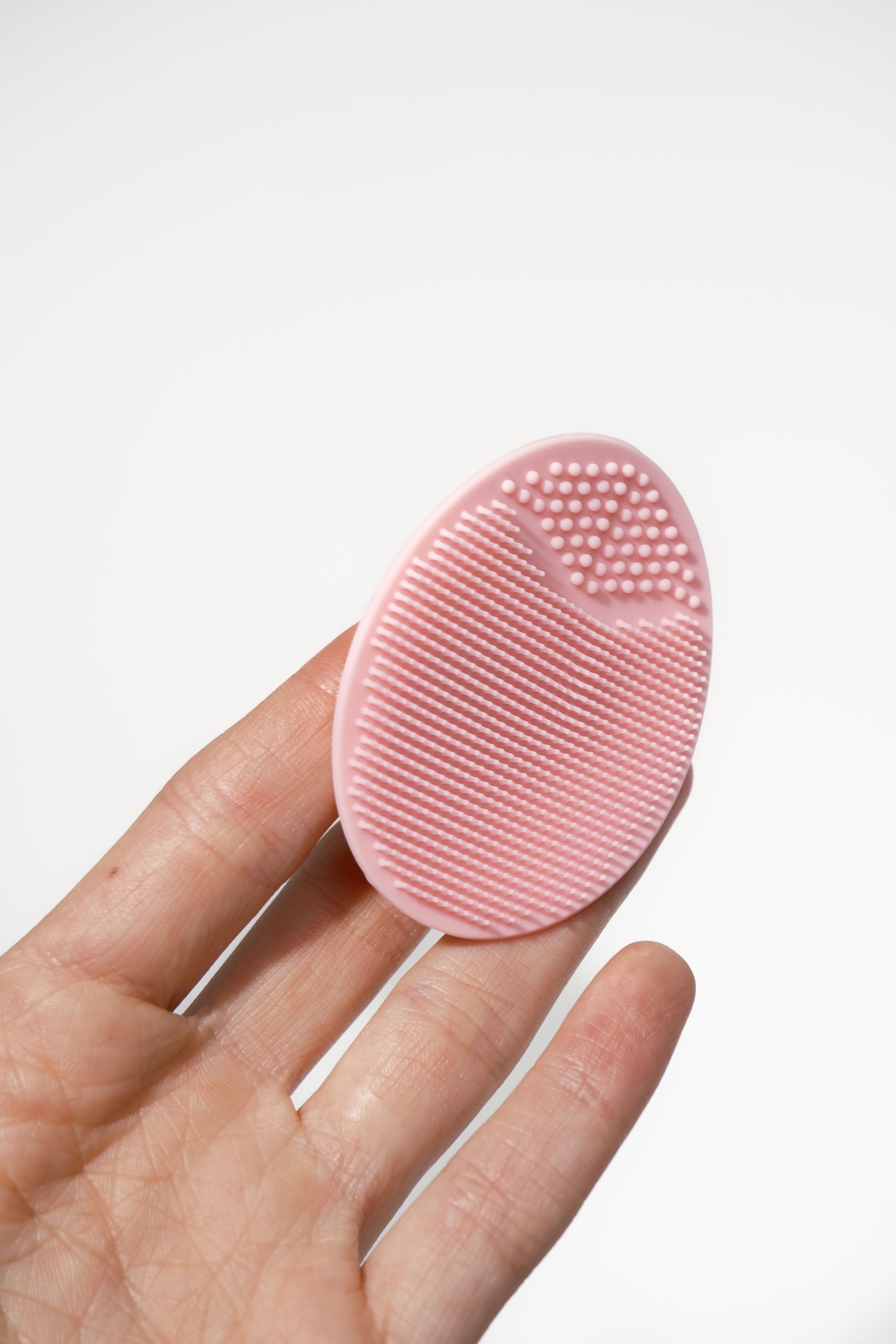 Roze siliconen gezichtsreinigingsborstel in een hand op een witte achtergrond