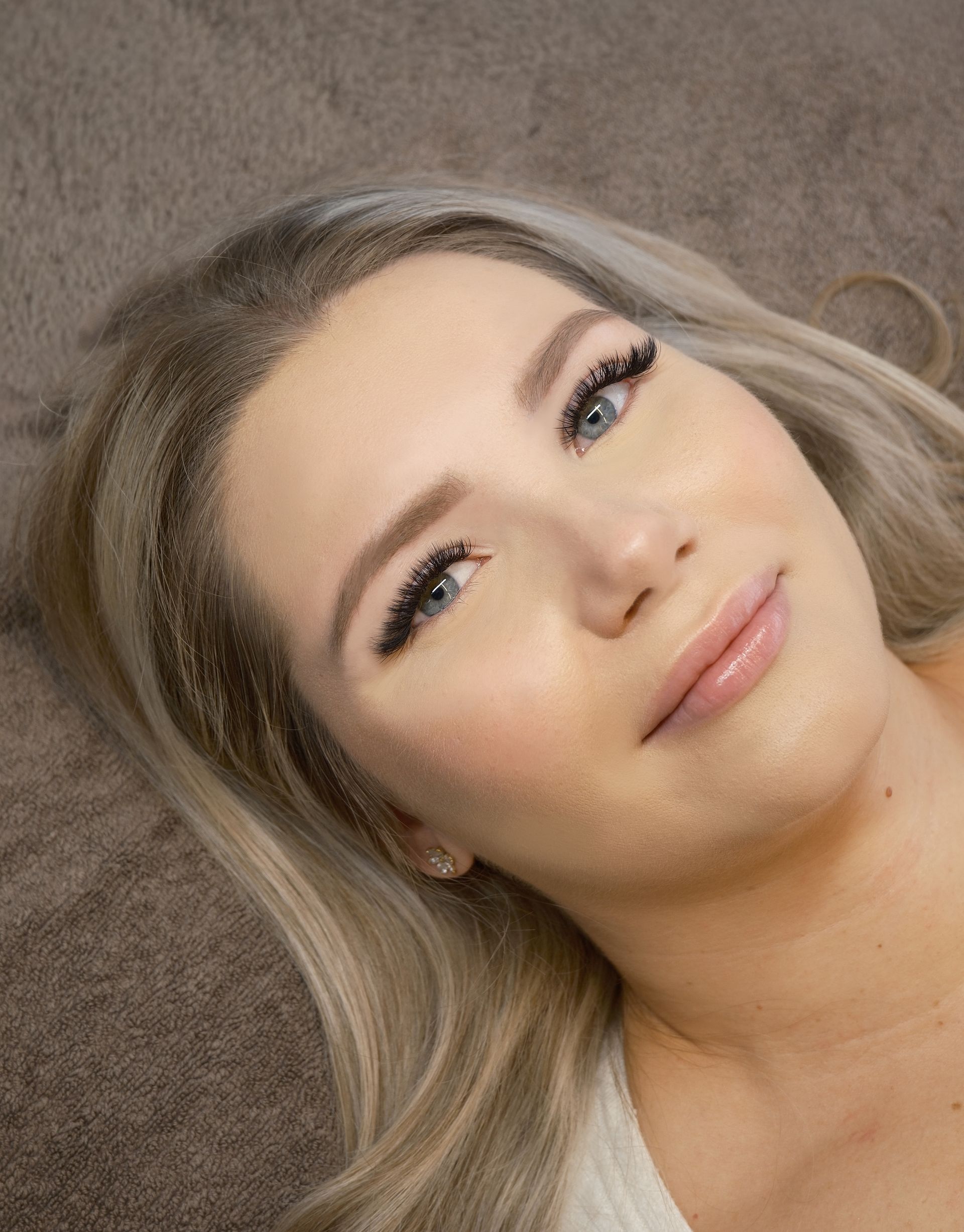 Close-up portret van een vrouw met blond haar, lichte make-up op een bruine achtergrond.