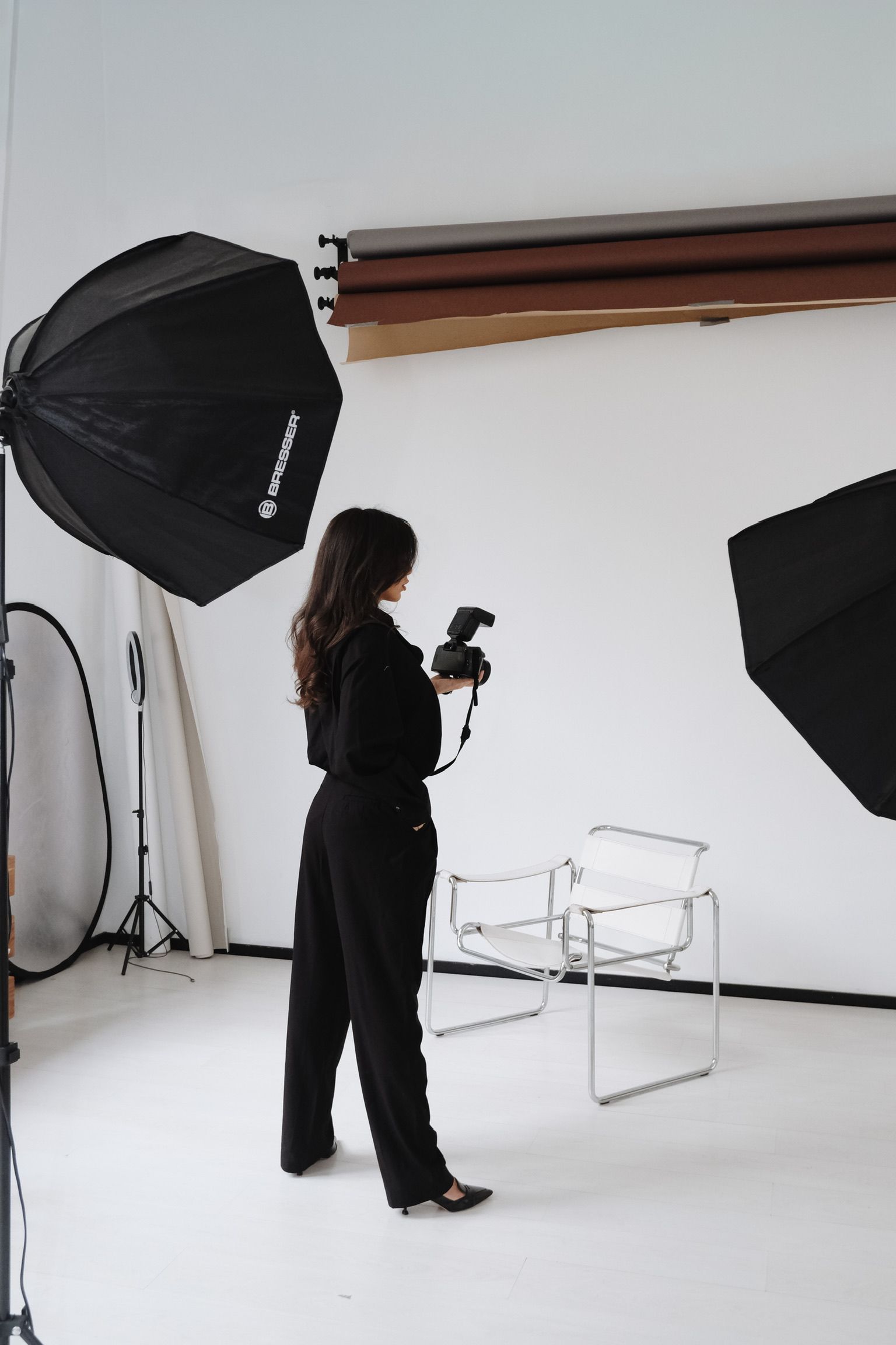 Persoon met een camera in een fotostudio met belichtingsapparatuur en een stoel.