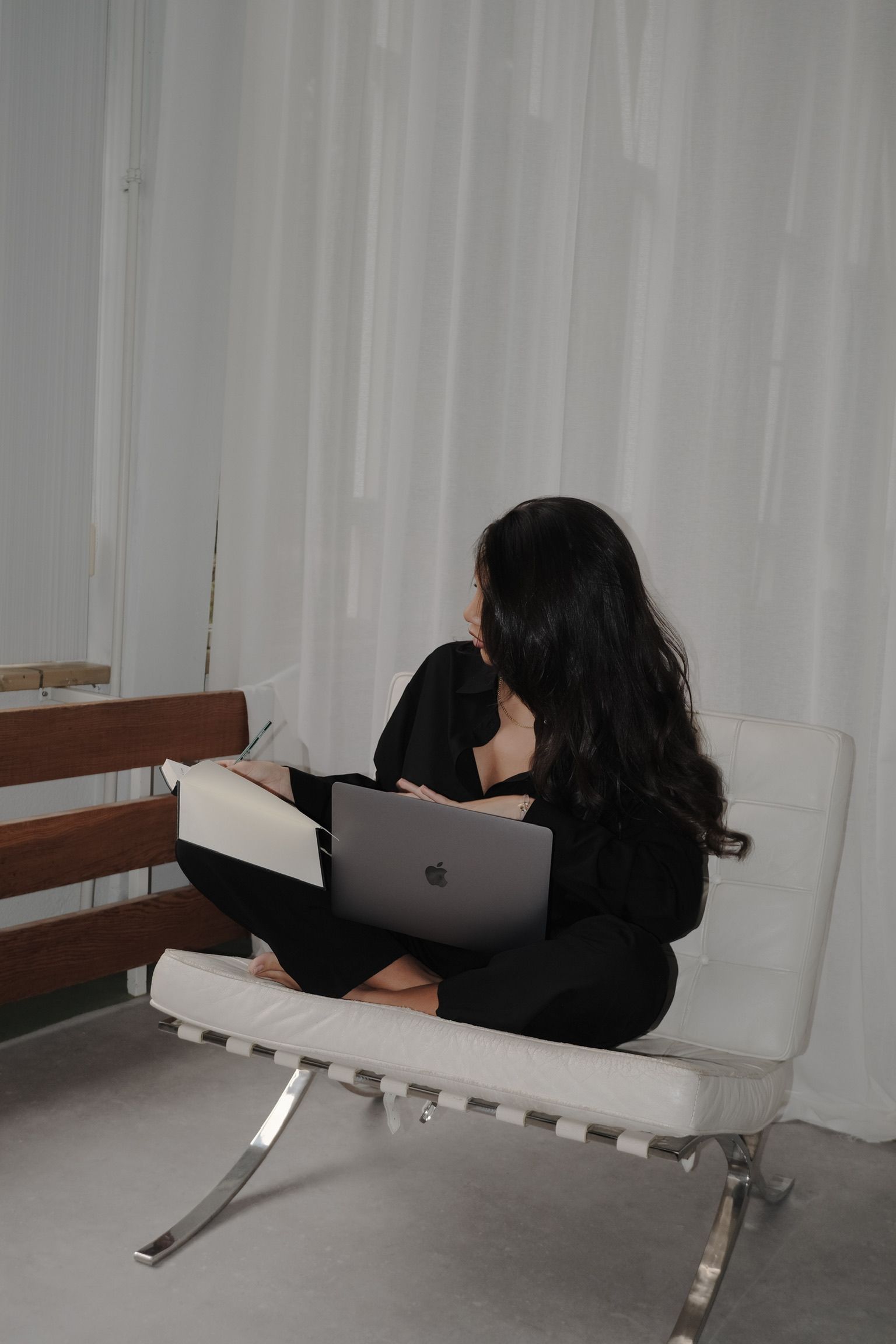 Een persoon zit op een witte stoel en gebruikt een laptop in een minimalistische kamer.