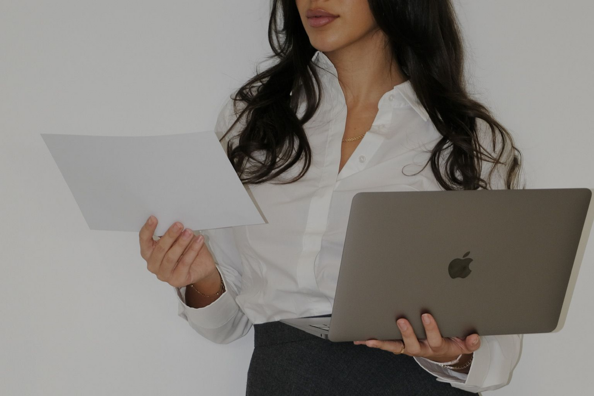 Vrouw in witte blouse met een opdracht en laptop tegen een witte achtergrond.