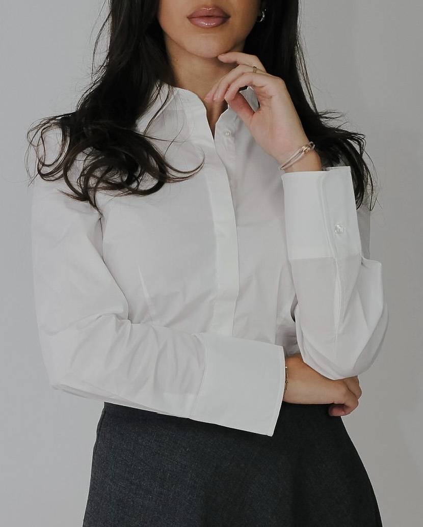 Vrouw in witte blouse en een donkere rok, poserend met één hand bij haar kin.