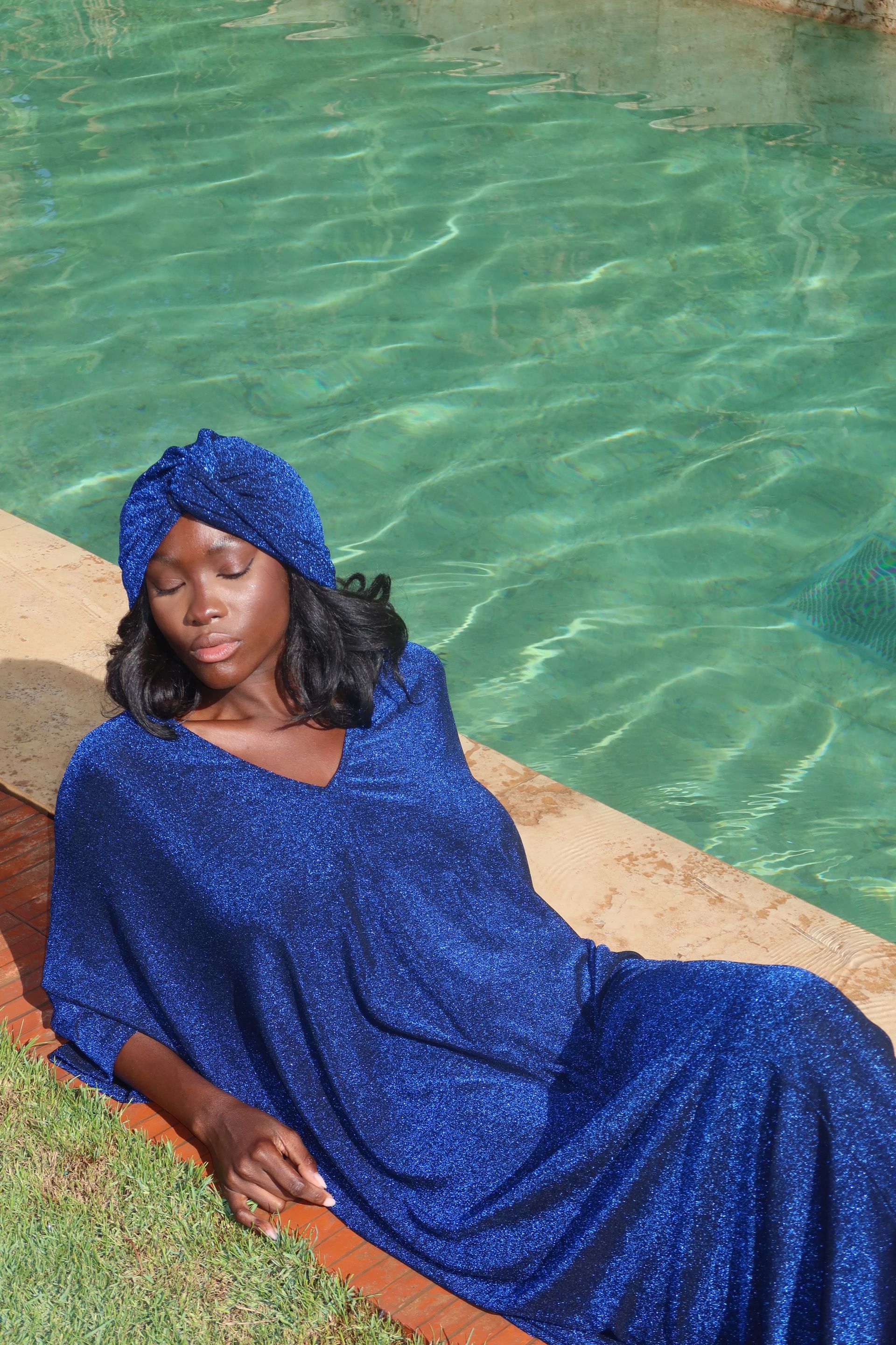 Vrouw in een glinsterende blauwe outfit, liggend naast een turquoise zwembad.