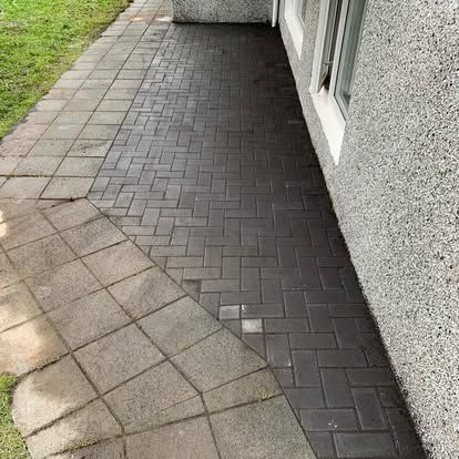 Múrsteinsverönd og gangstígur, hálfhreinsaður, við hliðina á byggingu með glugga.