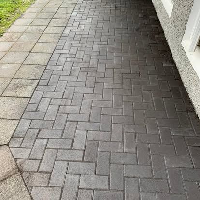 Múrsteinsgangur í síldarbeinsmynstri, við hliðina á steypuplötum og byggingu með hvítum köntum.