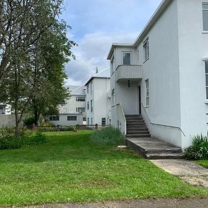 Hvítar byggingar með stiga og graslendi undir skýjuðum himni.