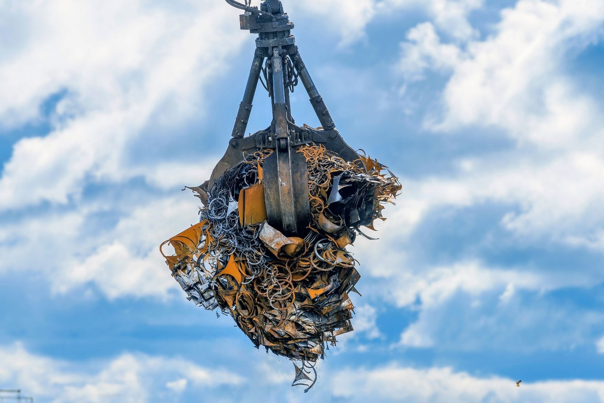 Grapple crane claw lifting a load of tangled rusty scrap metal and steel against a cloudy blue sky. Grapple crane claw lifting a load of tangled rusty scrap metal and steel against a cloudy blue sky.