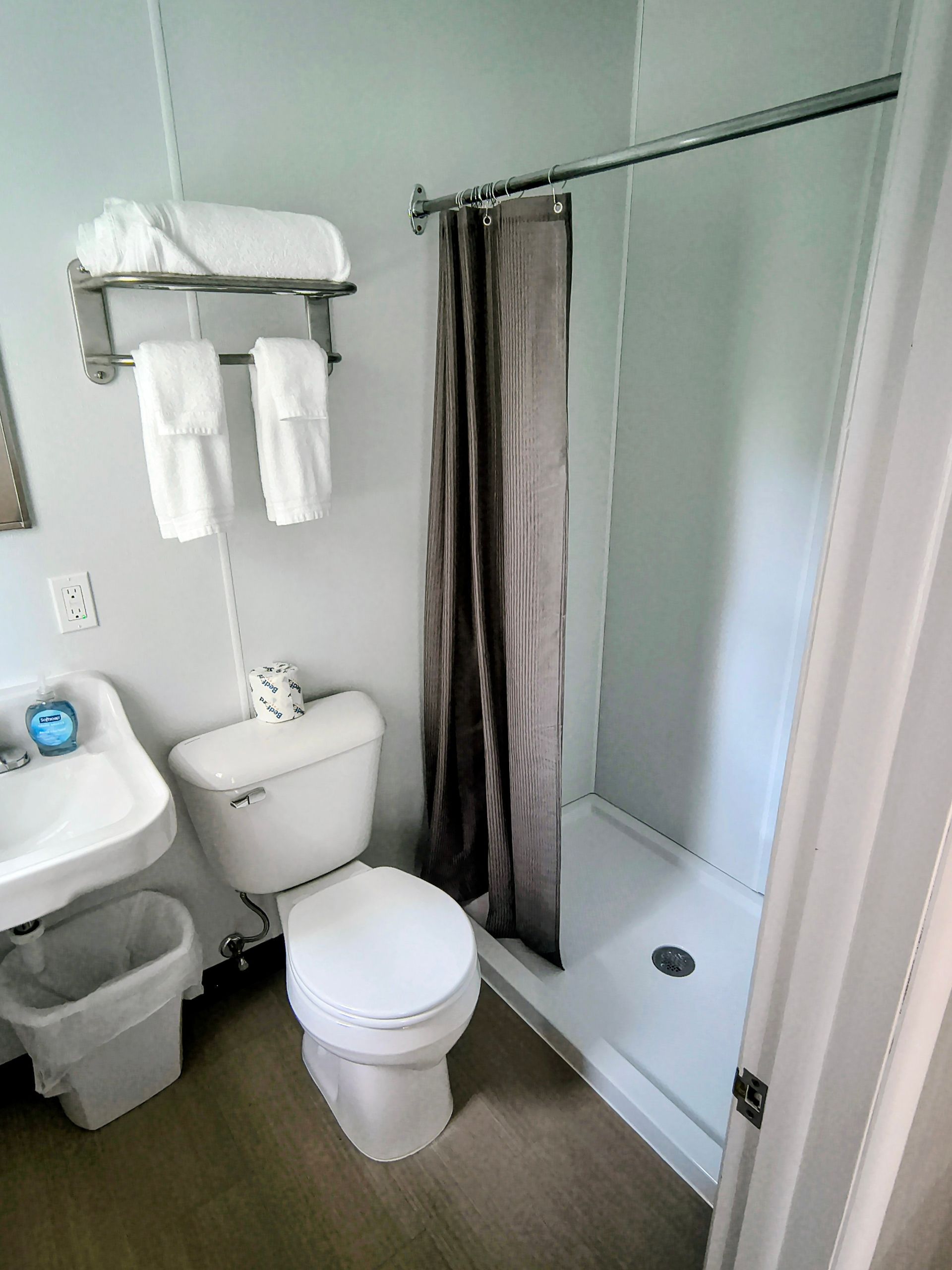 Small bathroom with toilet, sink, shower, and towel rack. White and gray color scheme.