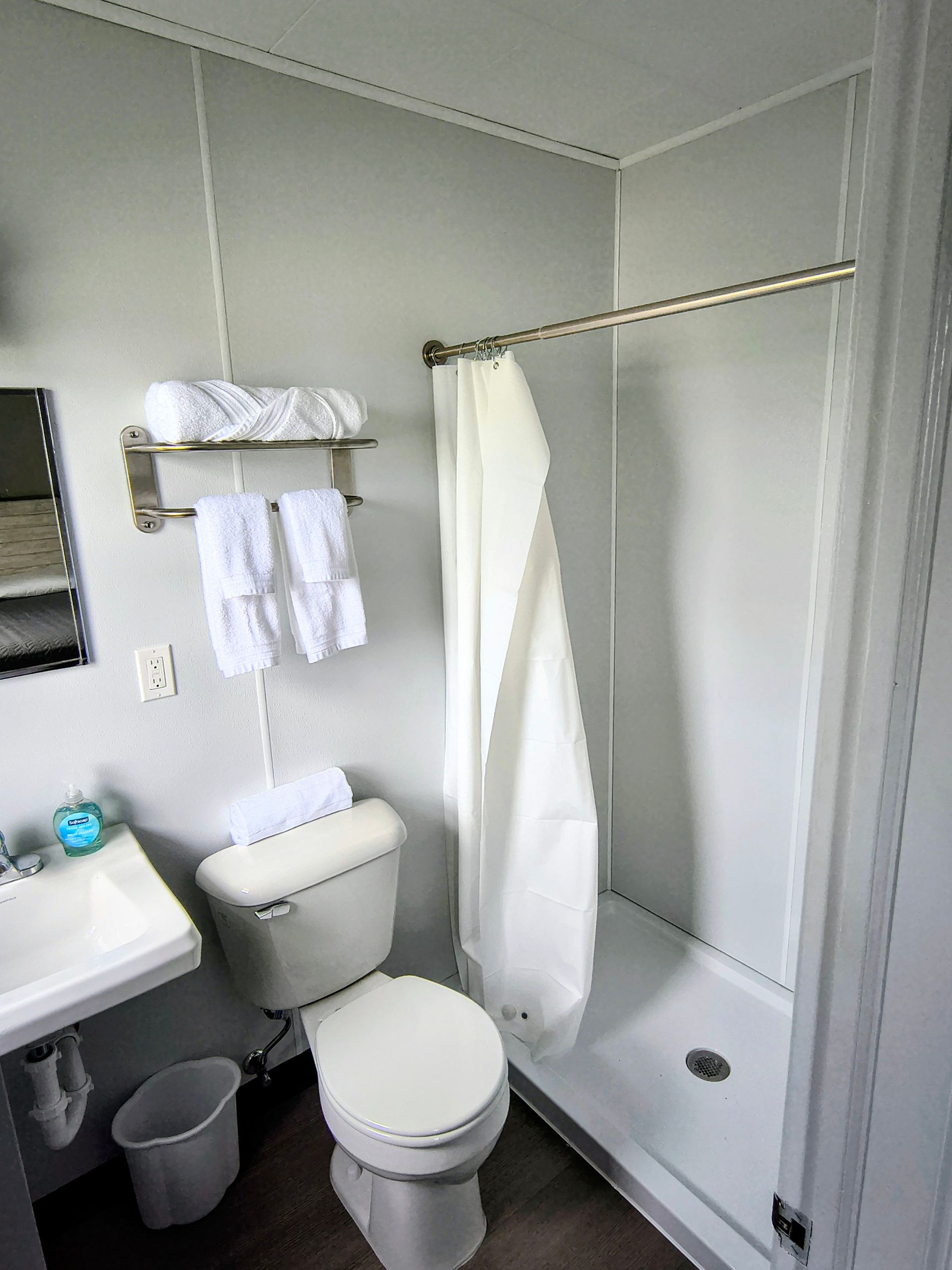 Small bathroom with a toilet, shower, sink, and towel rack. White walls and a white shower curtain.