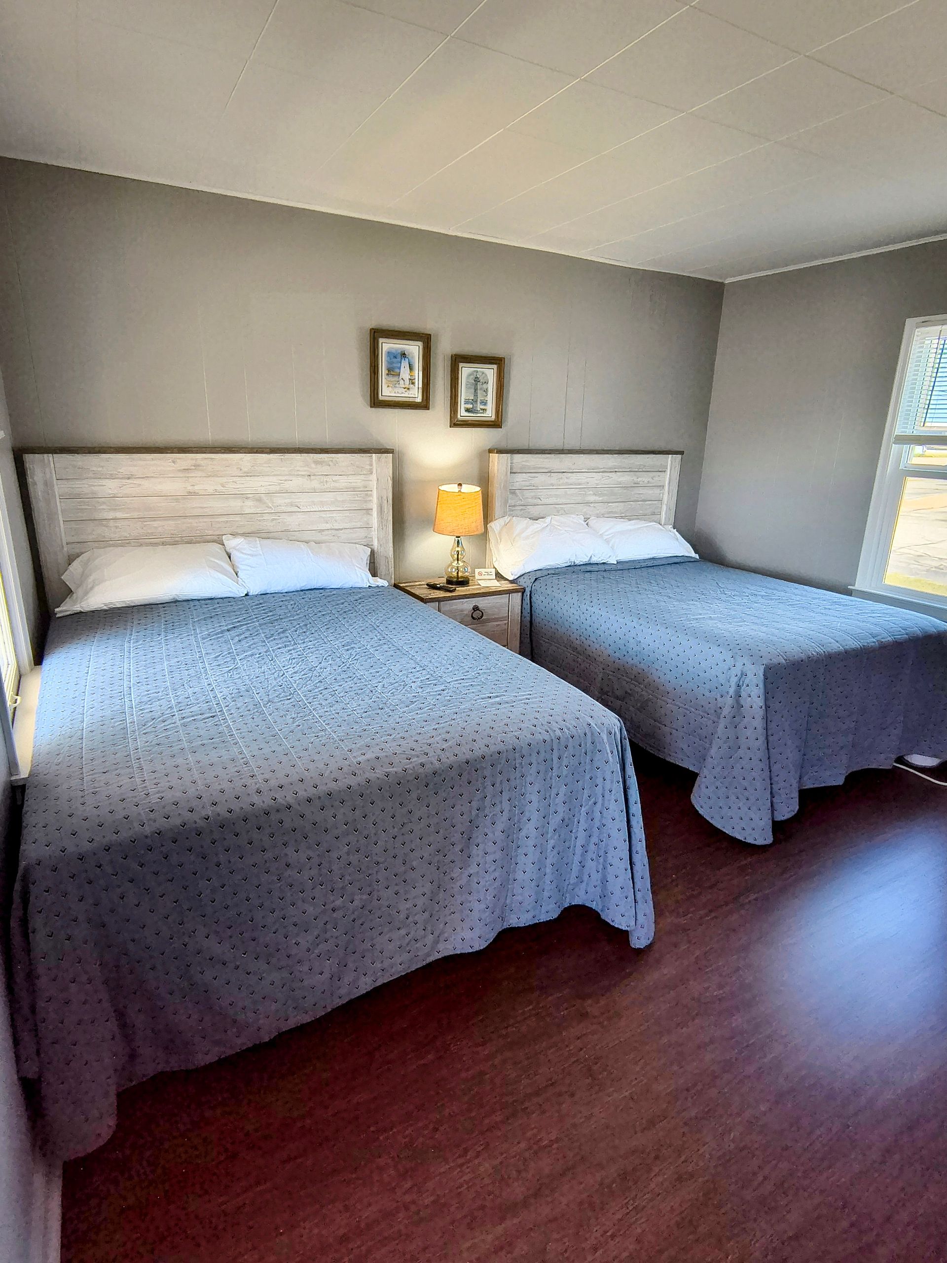 A hotel room with two twin beds covered in blue-grey patterned bedspreads. White headboards, nightstand with lamp