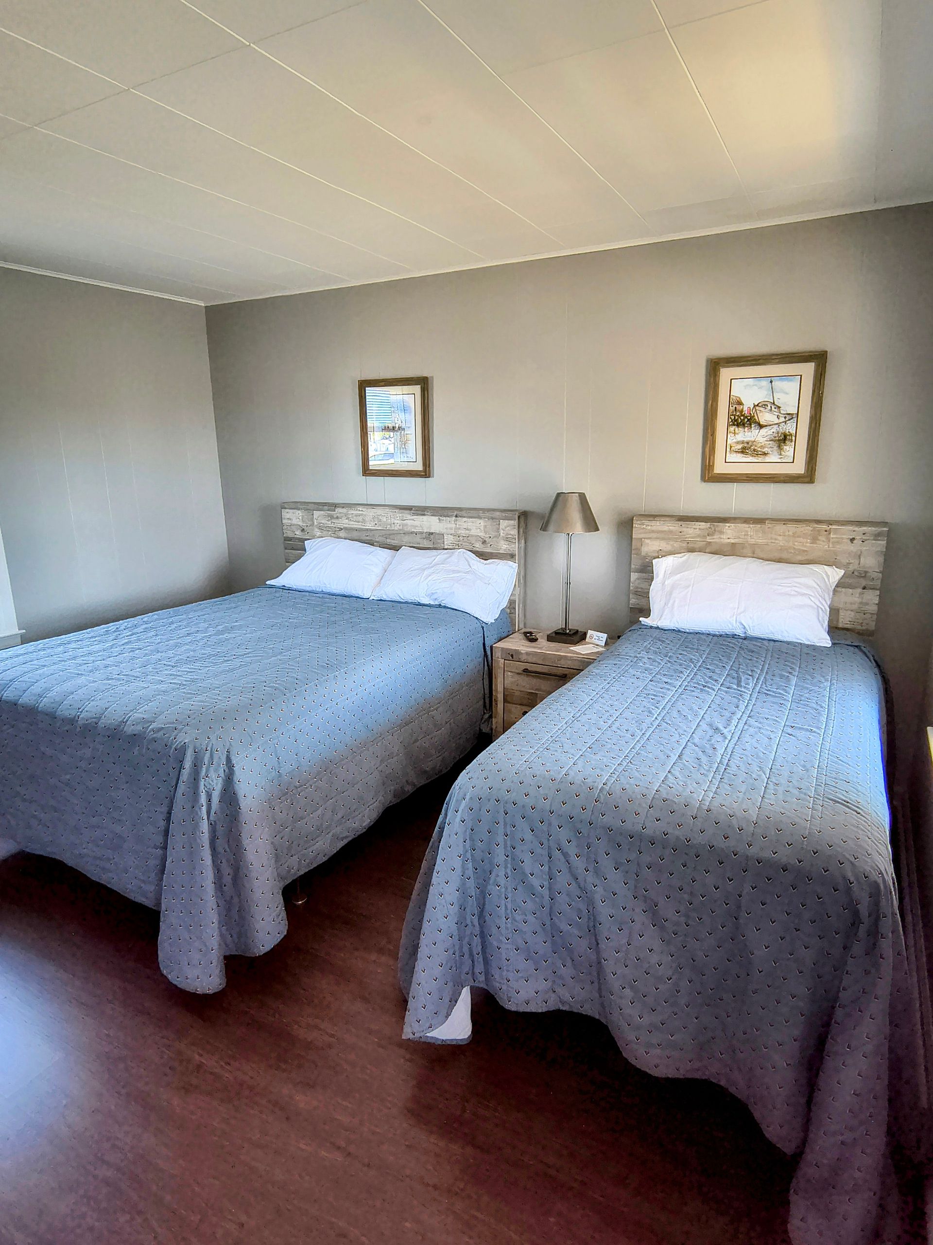 Two beds in a hotel room with gray walls. One double bed and one single bed with gray quilts.