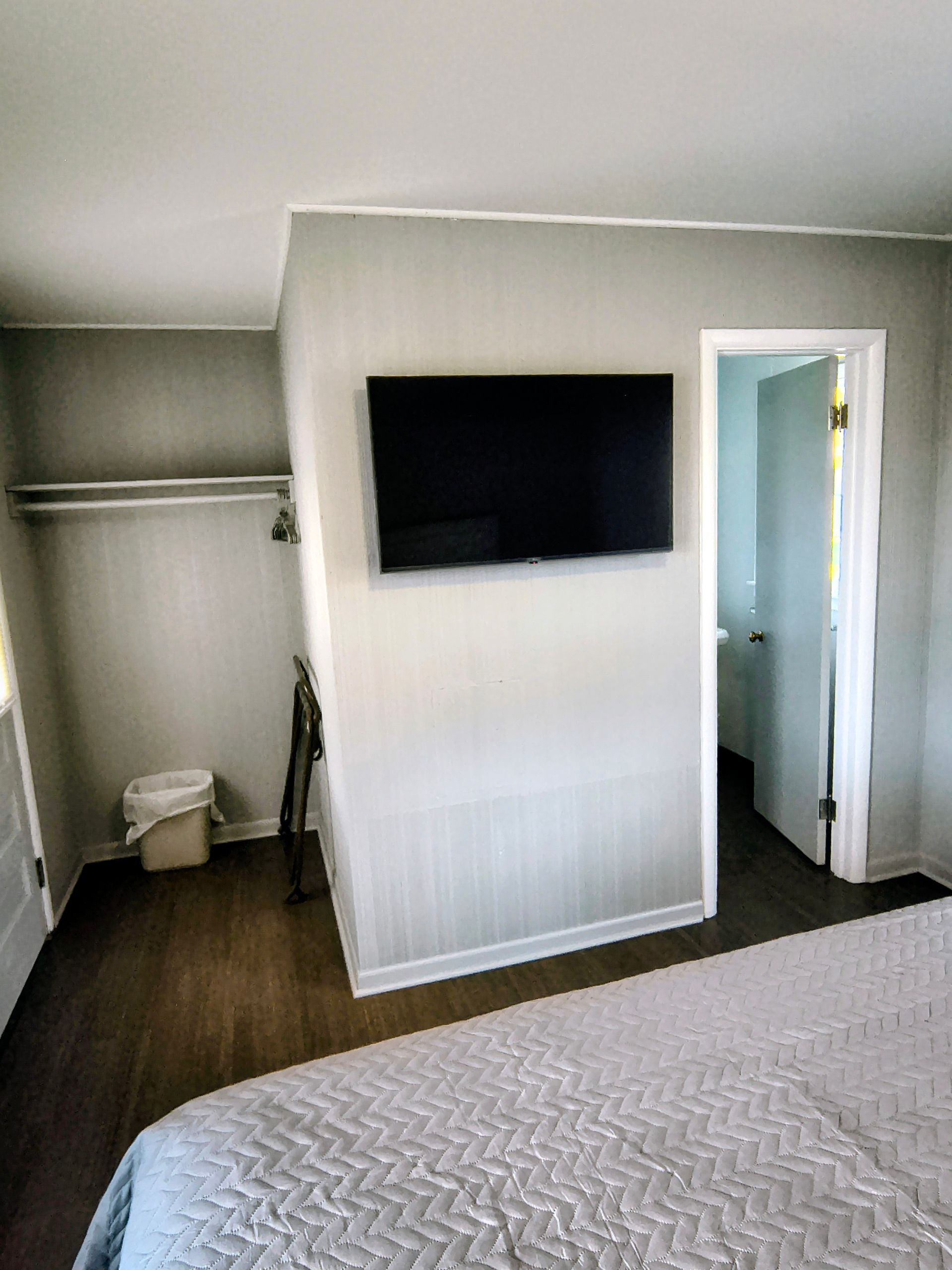 Bedroom with gray walls, TV, closet, and a bed covered in a gray quilt. The door to a bathroom is open.