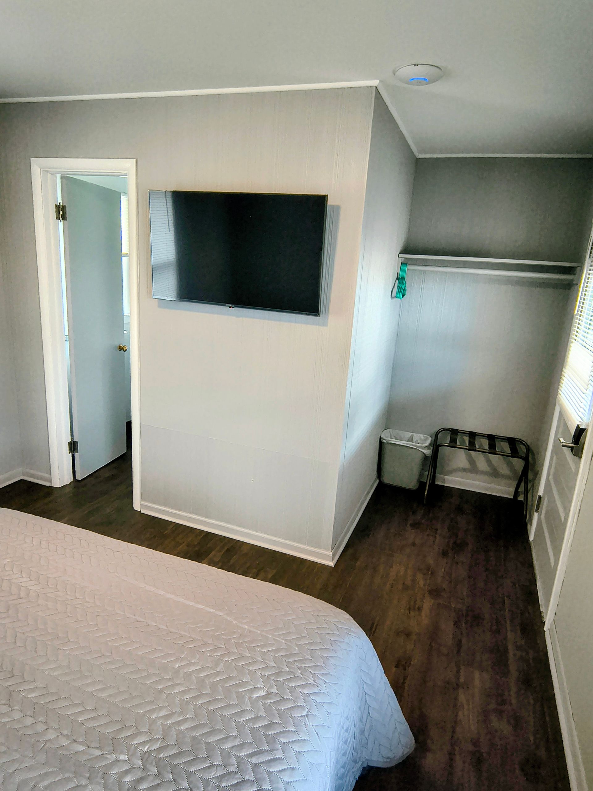 Bedroom with a TV in the wall, closet, door, and bed with a light gray cover.