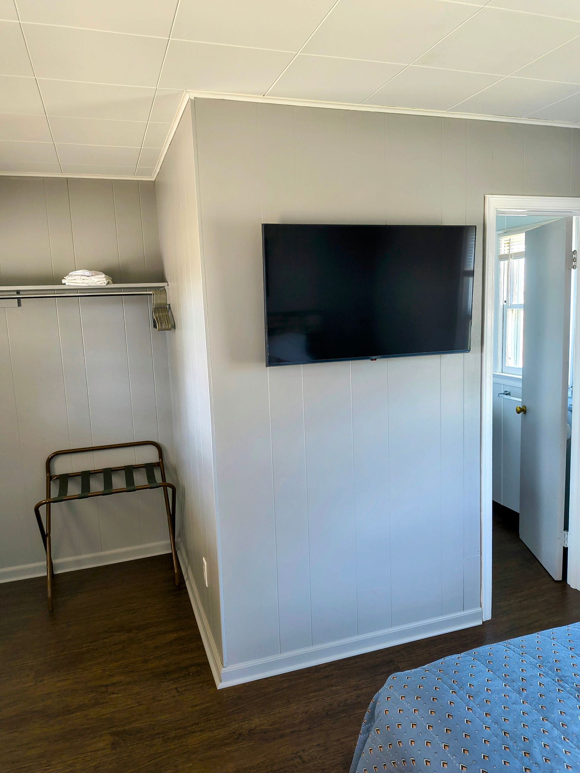 A small, rectangular television mounted on a light gray paneled wall in a room. A luggage rack sits below the TV.