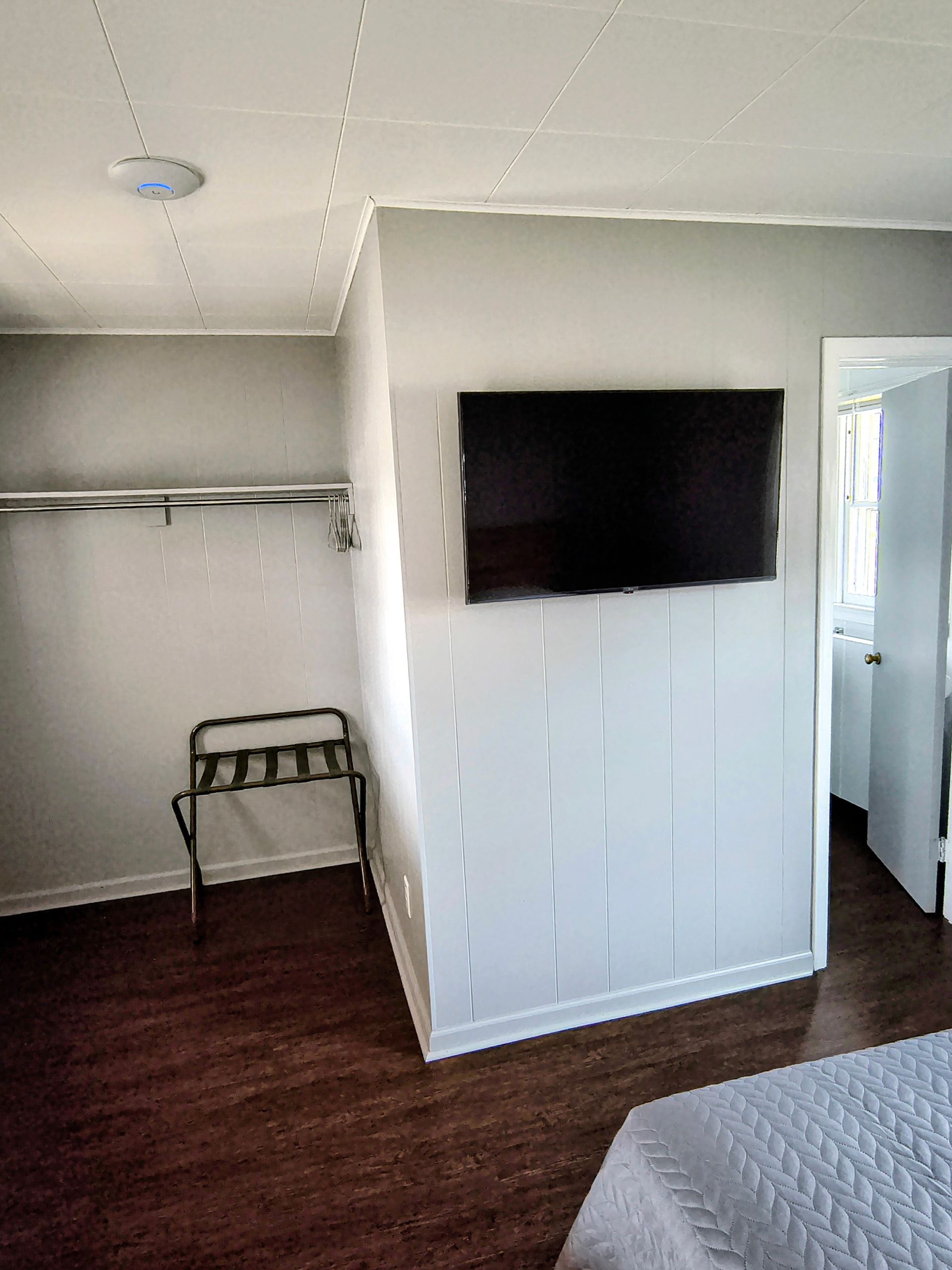 A hotel room with a mounted TV on a vertically paneled wall. There is a closet with a rack,