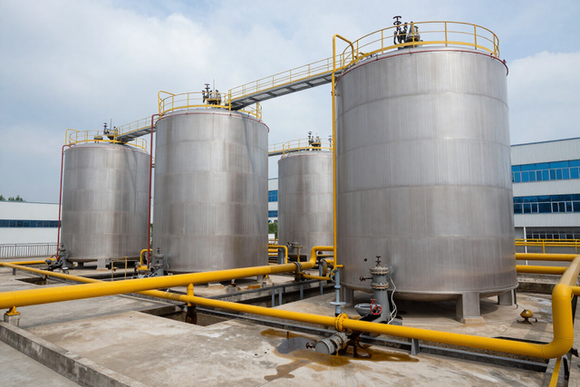 Grandes tanques de almacenamiento de acero inoxidable con tuberías industriales amarillas en una instalación al aire libre.