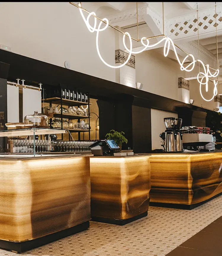 Modern café counter with glowing wood panels, hanging lights, and coffee equipment
