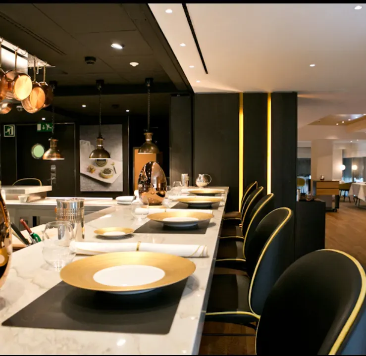 Modern restaurant interior with a marble bar, set tables, and black-and-gold chairs