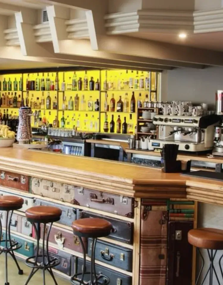 Stylish bar interior with yellow backlit shelves, wooden counter, stools, and a coffee machine