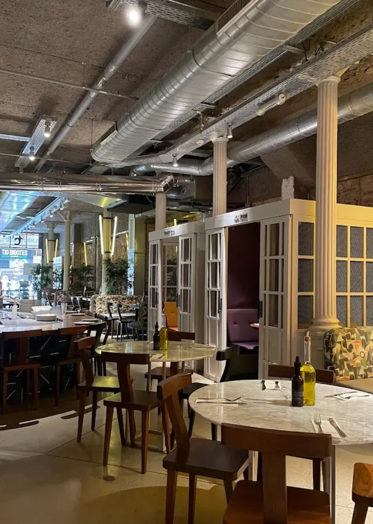 Empty restaurant dining area with wooden tables, chairs, and industrial ceiling ducts in warm light