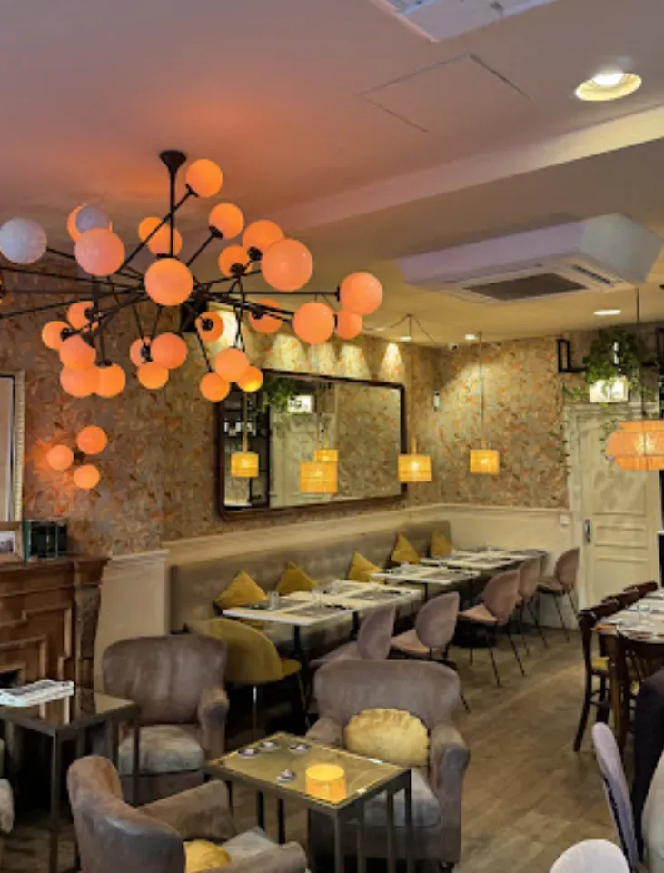 Cozy lounge with warm orange pendant lights, cushioned chairs, and small tables against textured walls.