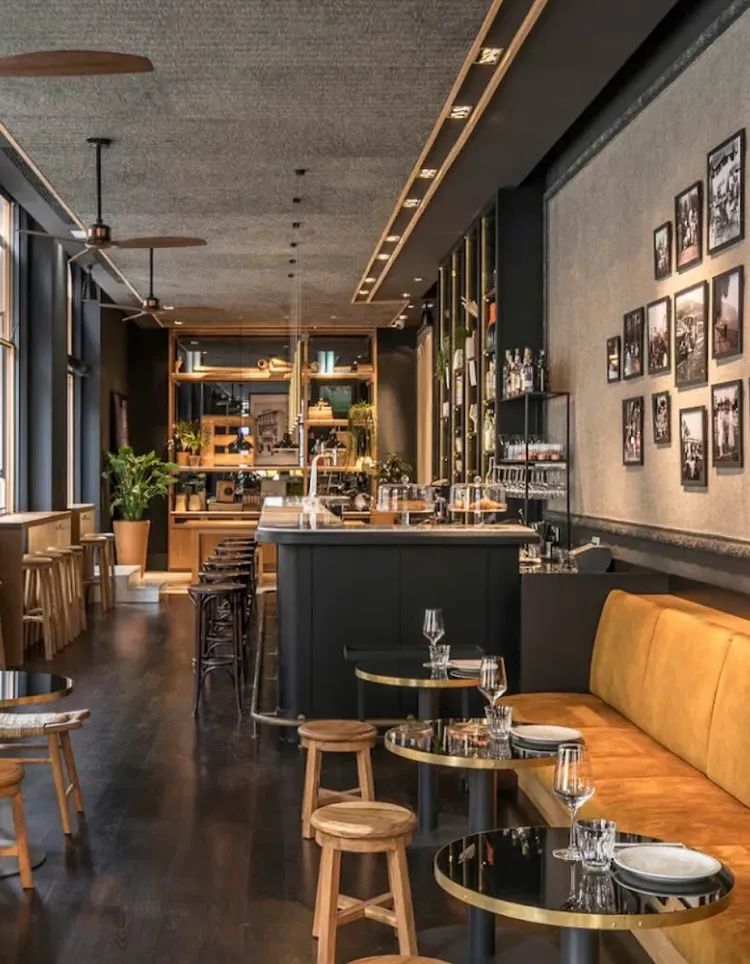 Modern café interior with dark wood floors, black tables, mustard bench seating, and a long bar