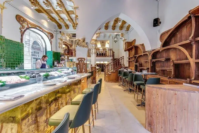 Bright café interior with gold decor, glass display case, bar stools, and arched windows