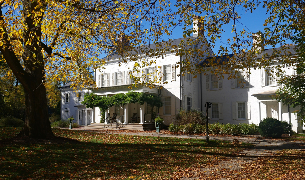 The front of Morven's colonial revival house and museum in fall, with leaves on the large grass lawn.