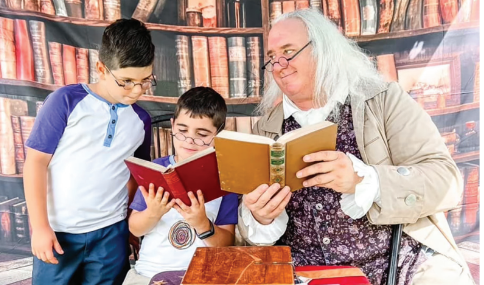 A historical reenactor portraying Benjamin Franklin reading to two young boys.