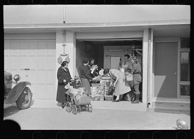 People unloading gifts from a car into a garage; a child sits in a stroller.