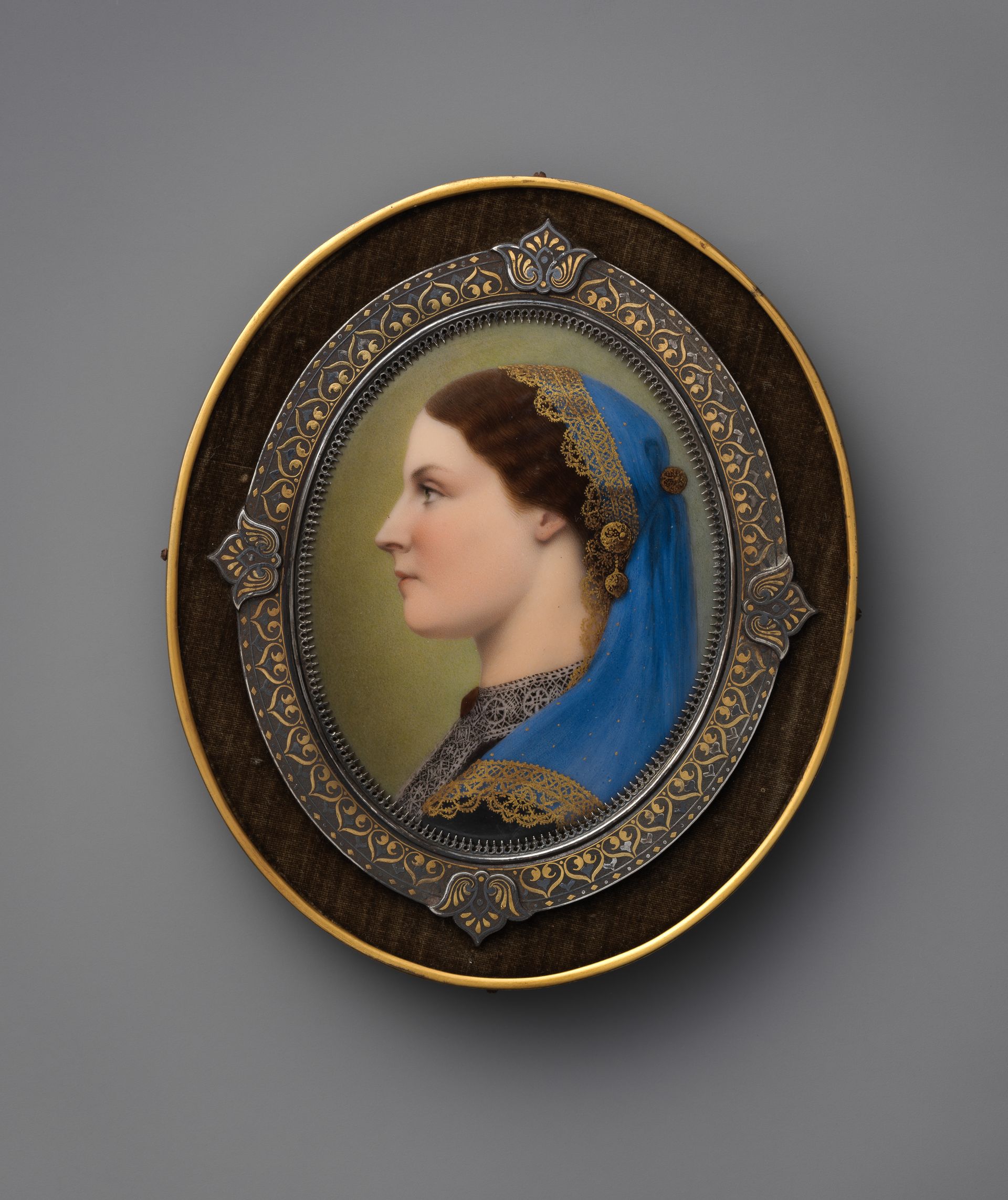 Oval portrait medallion of a woman in profile, framed in ornate gold and dark blue enamel.