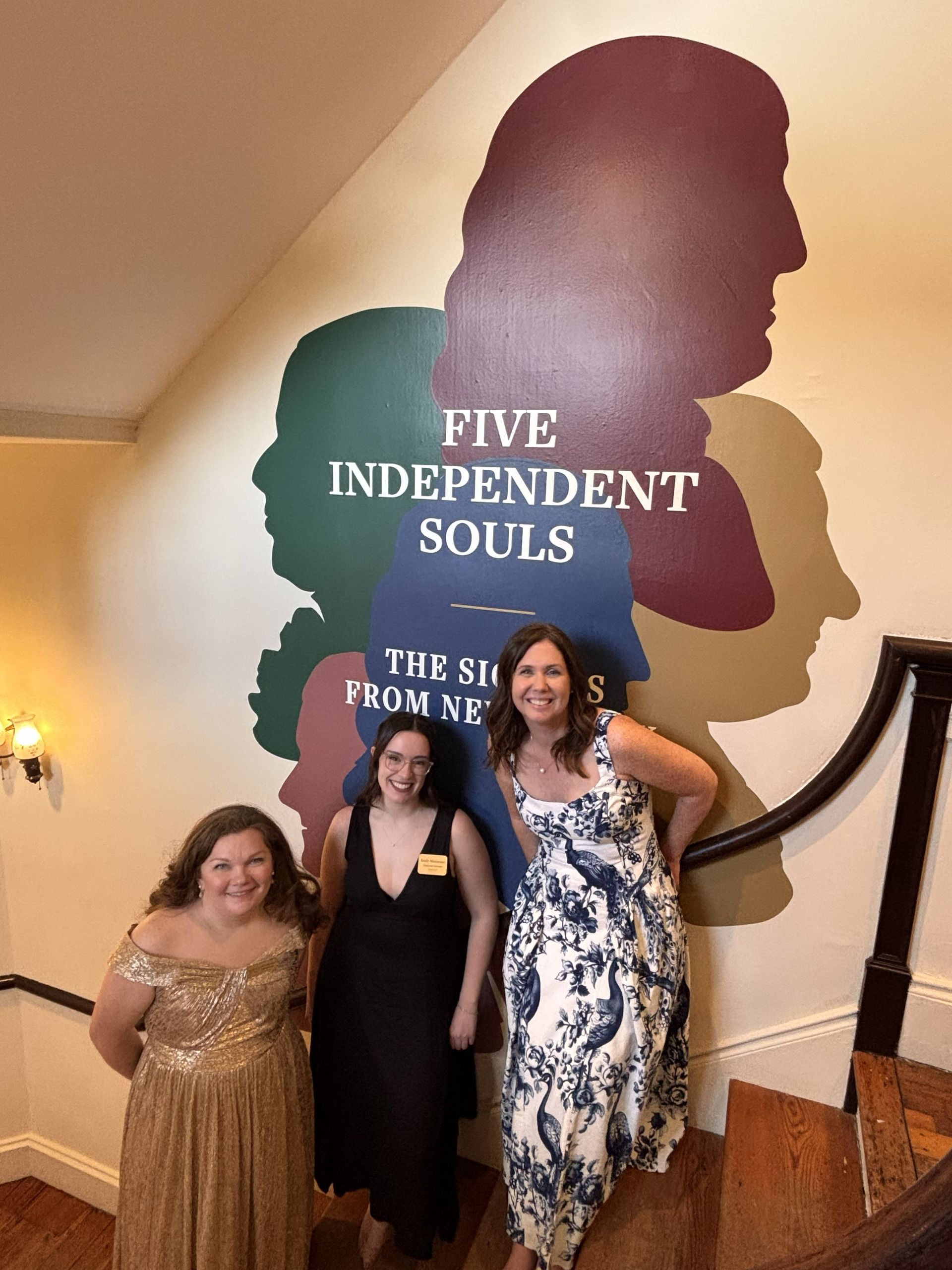 Three people posing indoors by a wall mural reading “Five Independent Souls.”