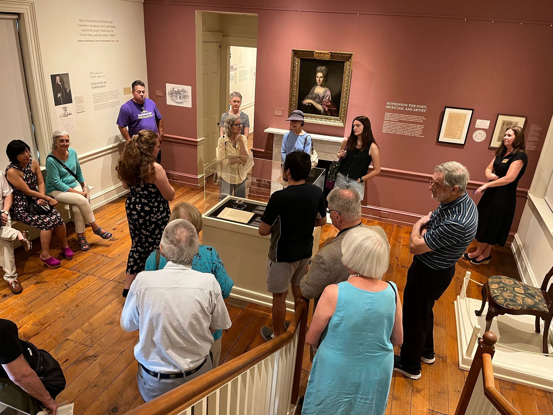 Museum group gathered around a guide in a gallery room with framed paintings and polished wood floors