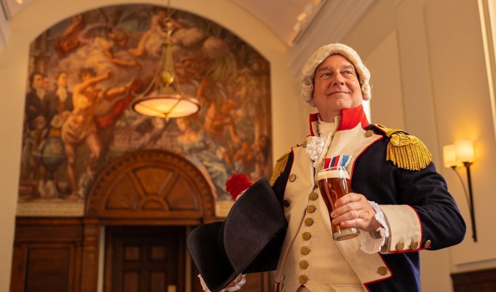 Historical reenactor in colonial dress holds a glass of beer and stands in Triumph Brewery in Princeton.