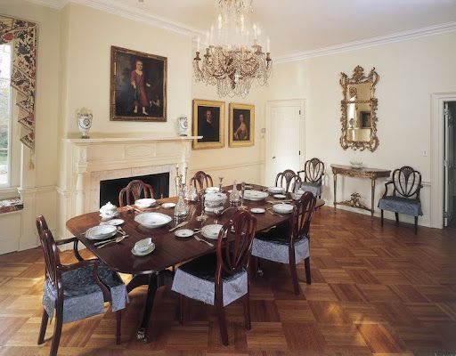Elegant dining room with oval table set for a meal, chandelier, fireplace, ornate mirror, and wood floor.