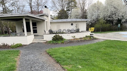 White house with a porch, patio, and pool in a grassy yard. Trees with white blossoms in the background.