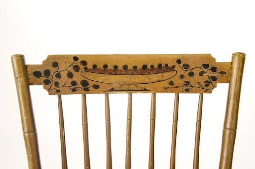 Close-up of a chair backrest with painted floral and boat designs on a light-colored wooden surface.