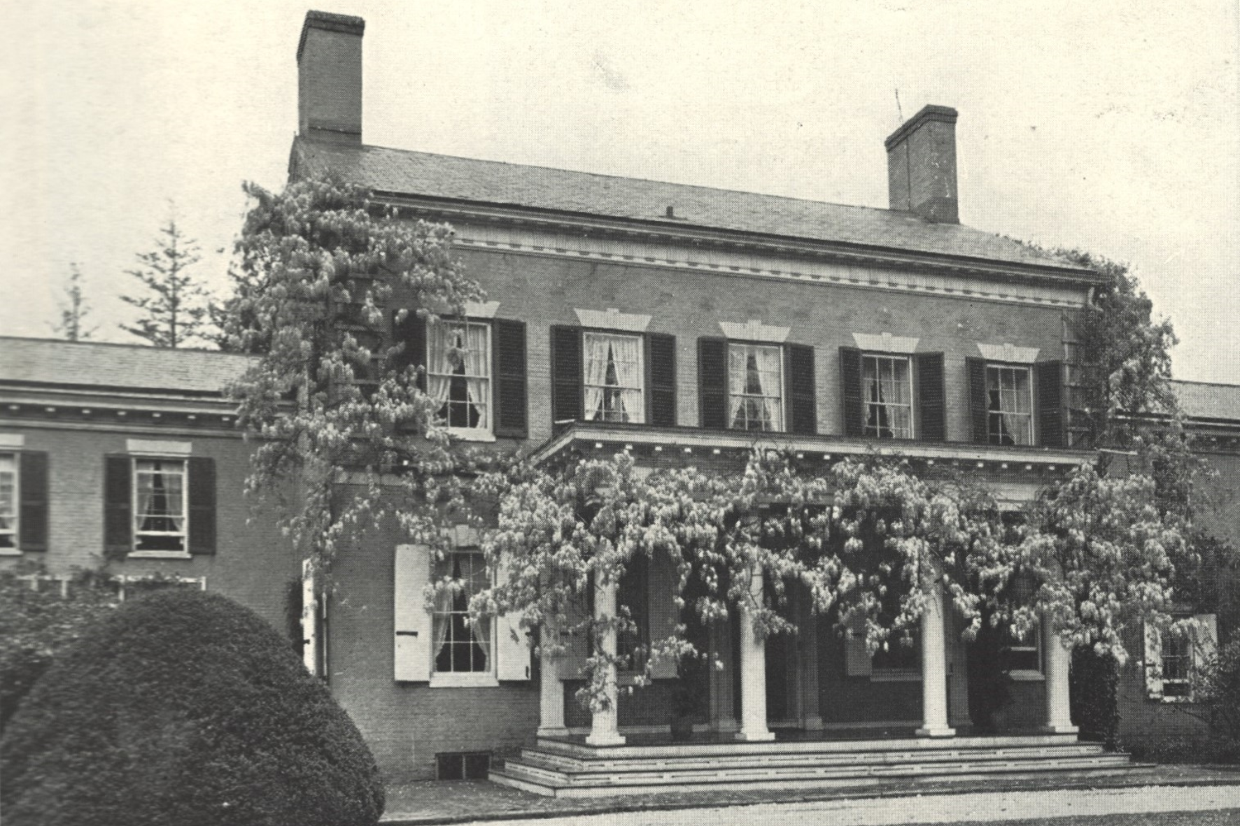 Two-story, colonial-style house with pillars, vines, and black shutters on the windows.