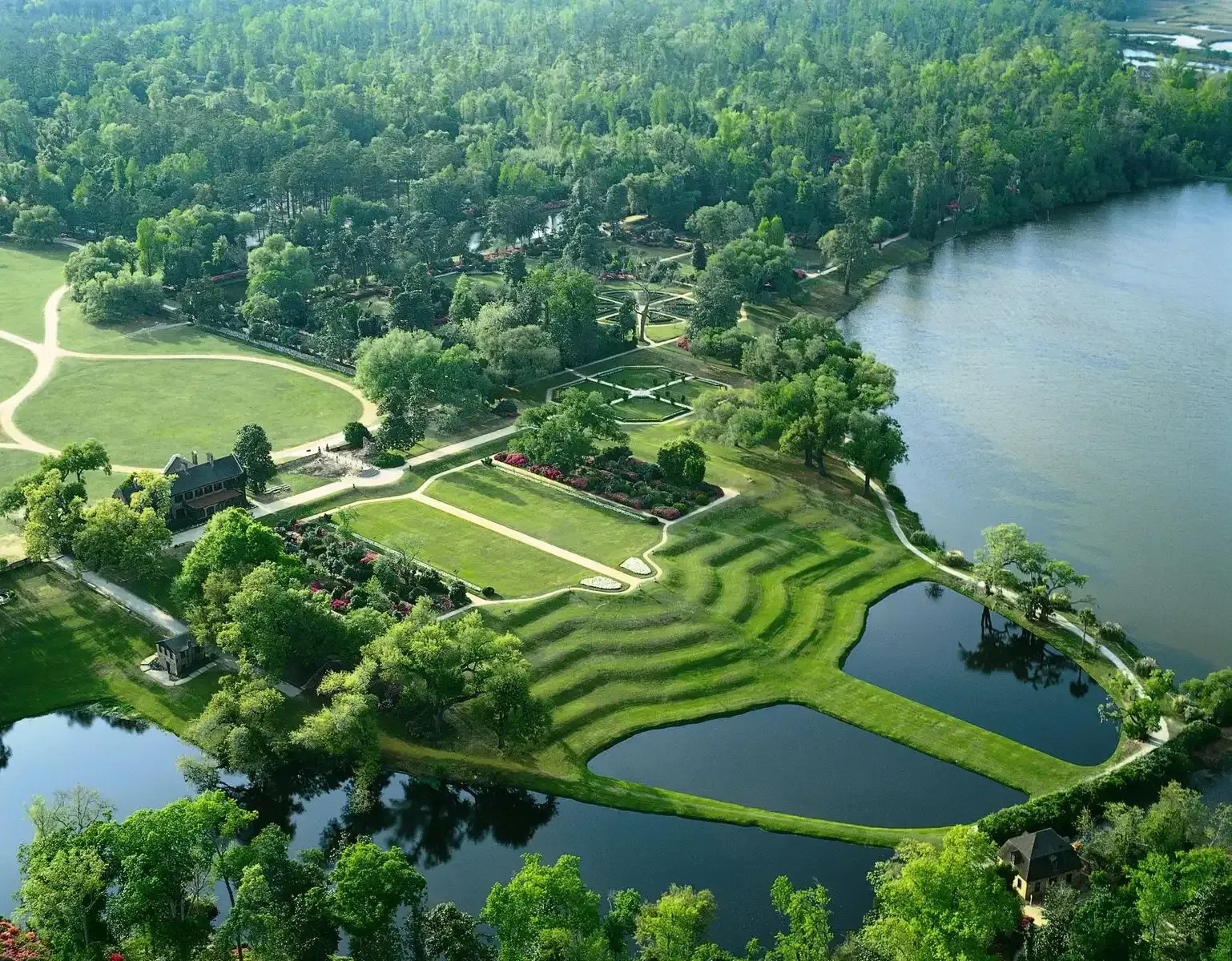 Aerial view of Middleton Place gardens, featuring terraced grassy slopes leading down to ponds next to the Ashley River.